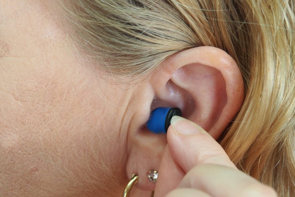 image of custom-made invisible hearing device being placed in ear of female patient